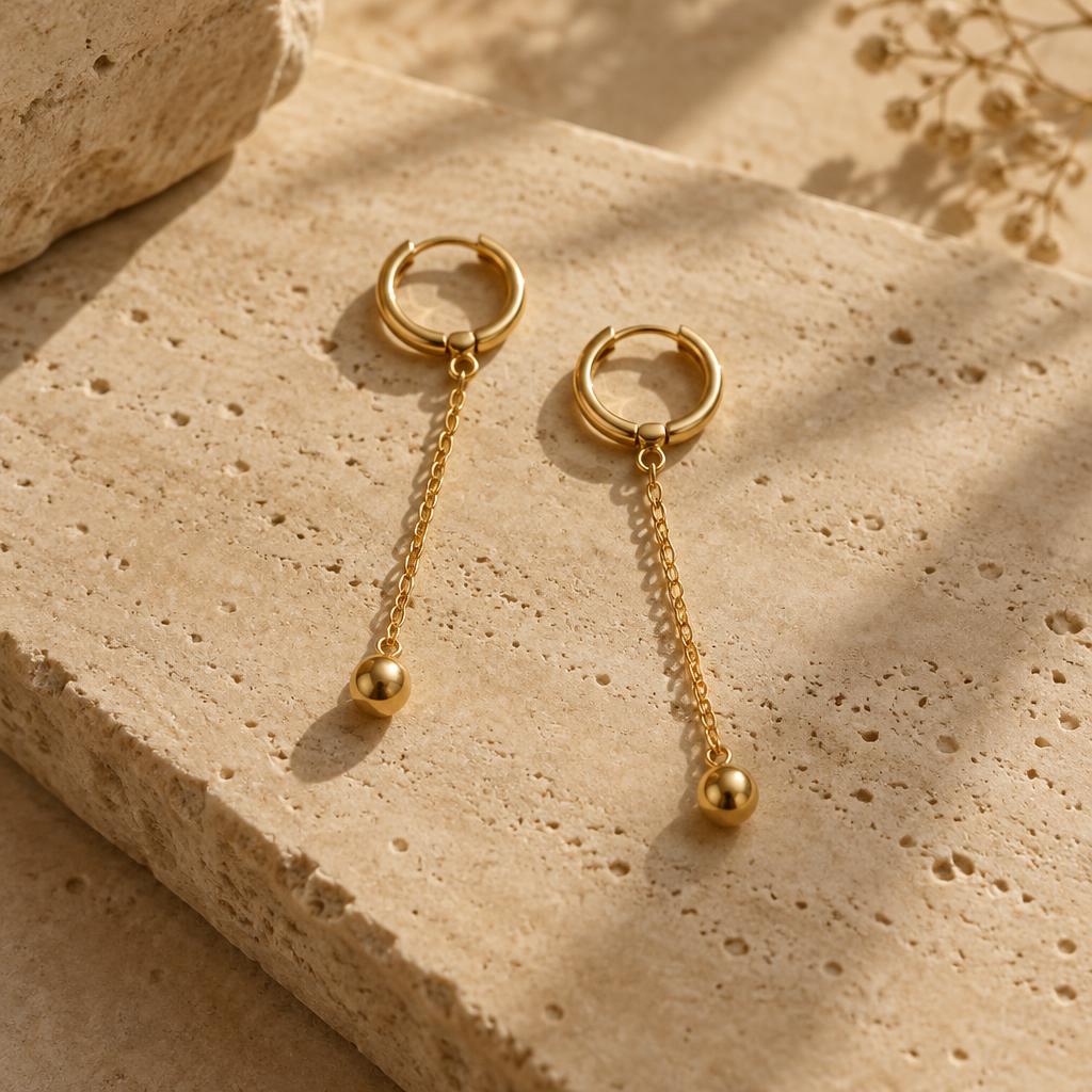 Gold chain drop earrings on warm travertine stone